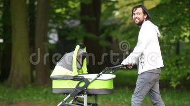 一位年轻的父亲带着婴儿车在公园里散步。 有新生婴儿的男人。 亲子关系。 嬉皮士。 父亲节`